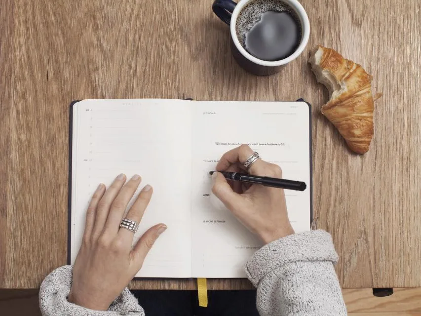 Aantekeningen in een notitieboek naast koffie en een croissant